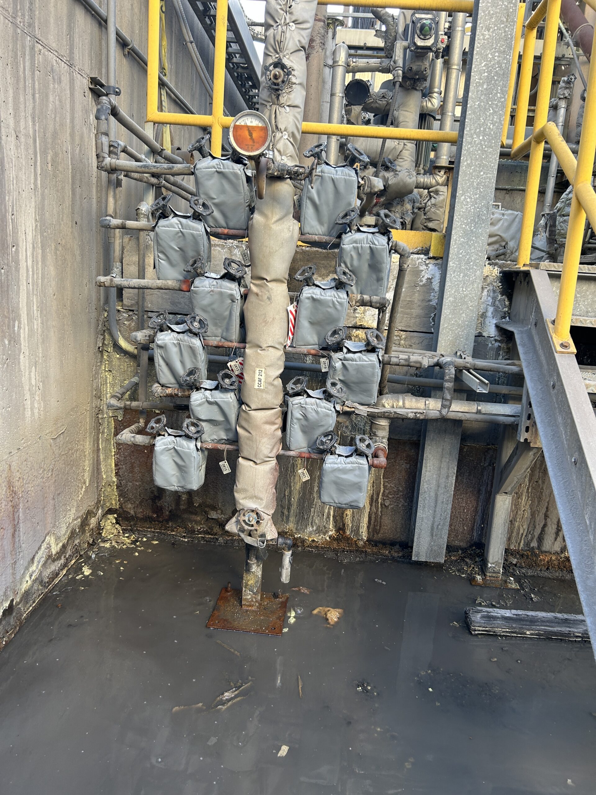 Industrial pipes covered with grey insulation jackets and yellow tags in a clean, orderly setting, indicating a chilled water system.